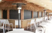 Sleek motorized roll-down shutters by Alutech installed around an outdoor kitchen and pool bar, providing privacy, weather protection, and easy operation.