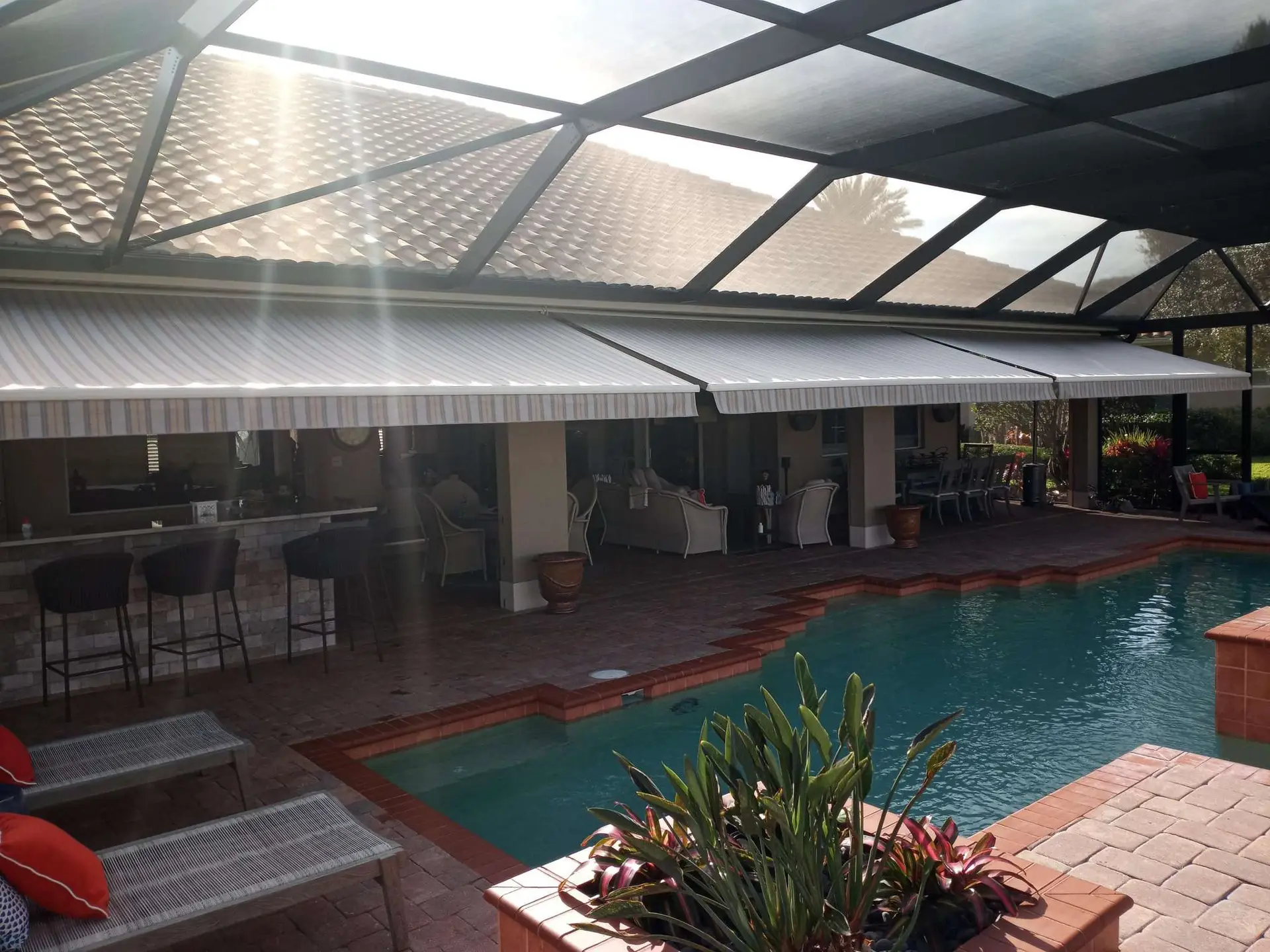 Motorized retractable screen enclosure over a pool lanai providing shade, privacy, and insect protection in a Florida home.
