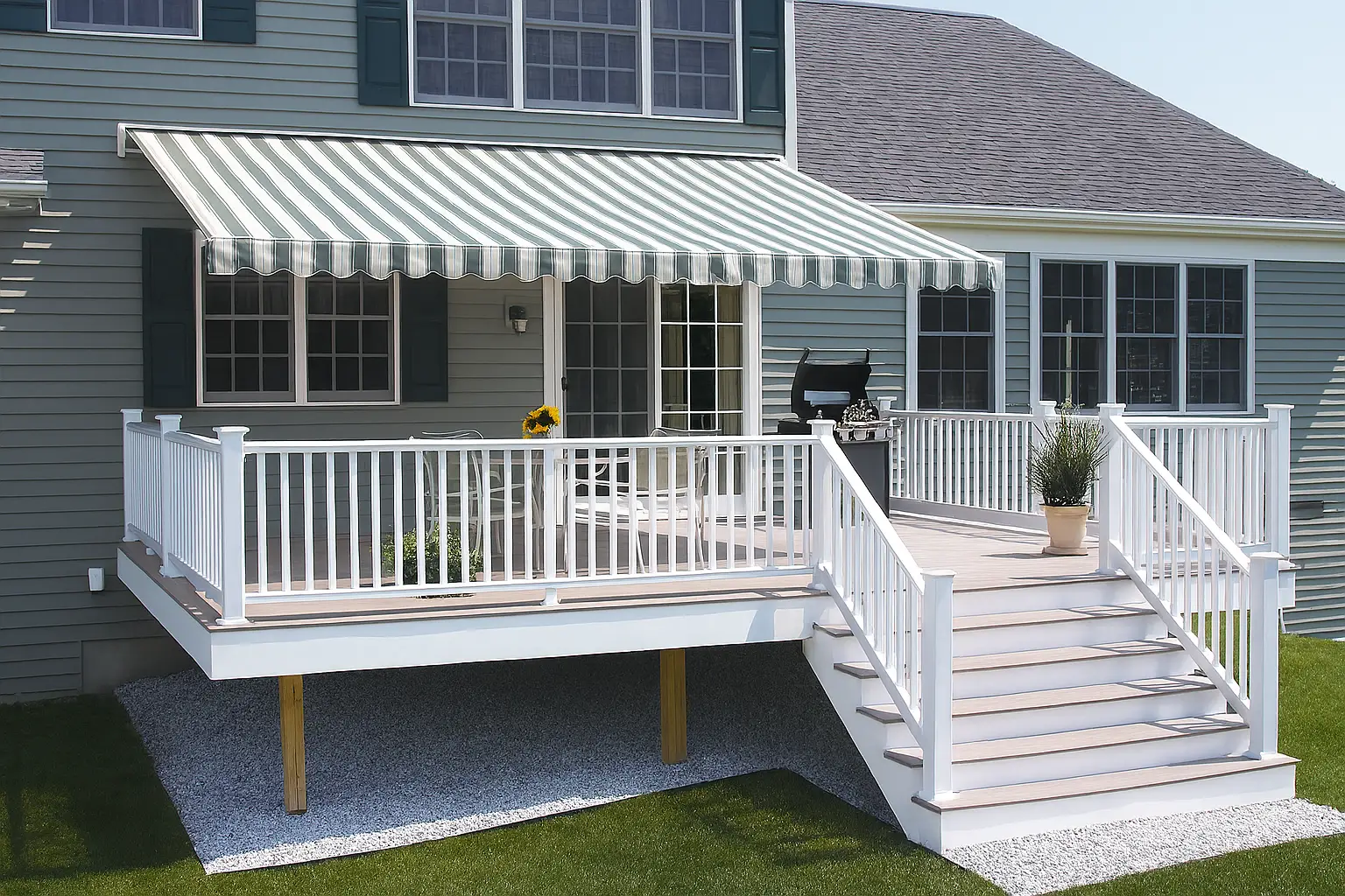 Green-and-white striped retractable awning over a white-railed deck with outdoor dining and grill setup.