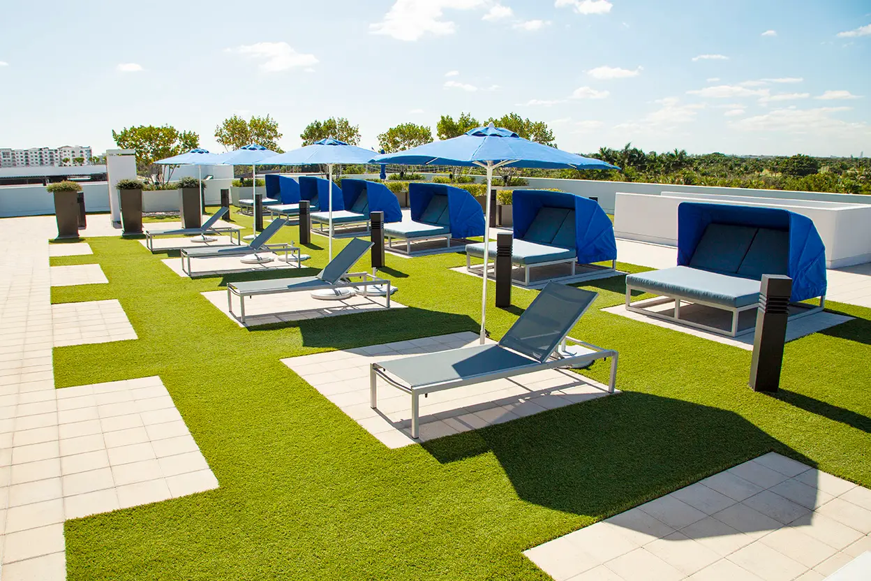 Poolside lounge area with cushioned chairs, umbrellas, and a clear blue pool surrounded by landscaped greenery.